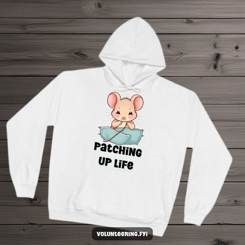 Funny mouse hoodie, showing a happy mouse sewing a patch onto fabric with a tiny needle and thread, a cozy humorous gift.