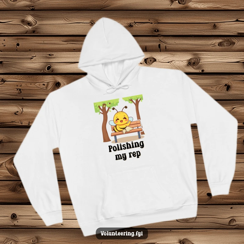 Funny Hoodie: Joyful yellow bee with a determined expression polishes a park bench with a small cloth, warm and diligent.